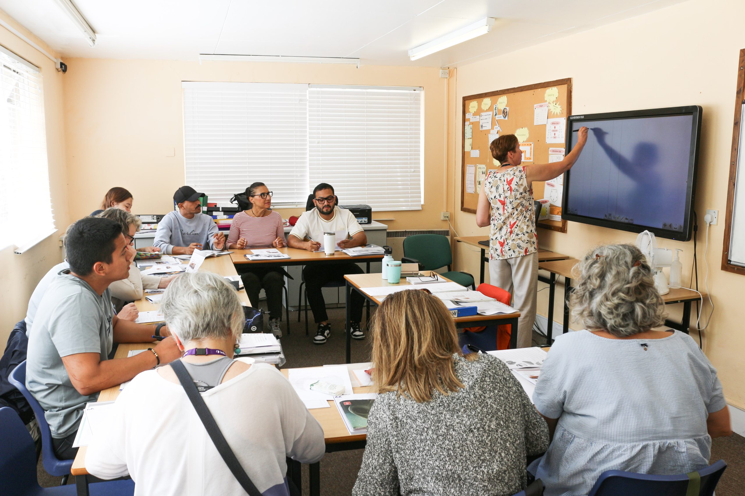 A small group of adult students working with their teacher around a table in a classroom at inlingua Cheltenham