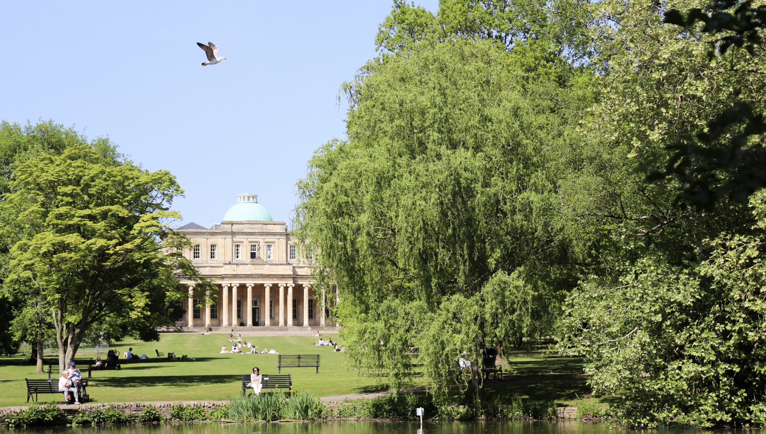The Pittville Pump Room in Cheltenham, a Regency building with a domed roof and colonnade, seen across parkland